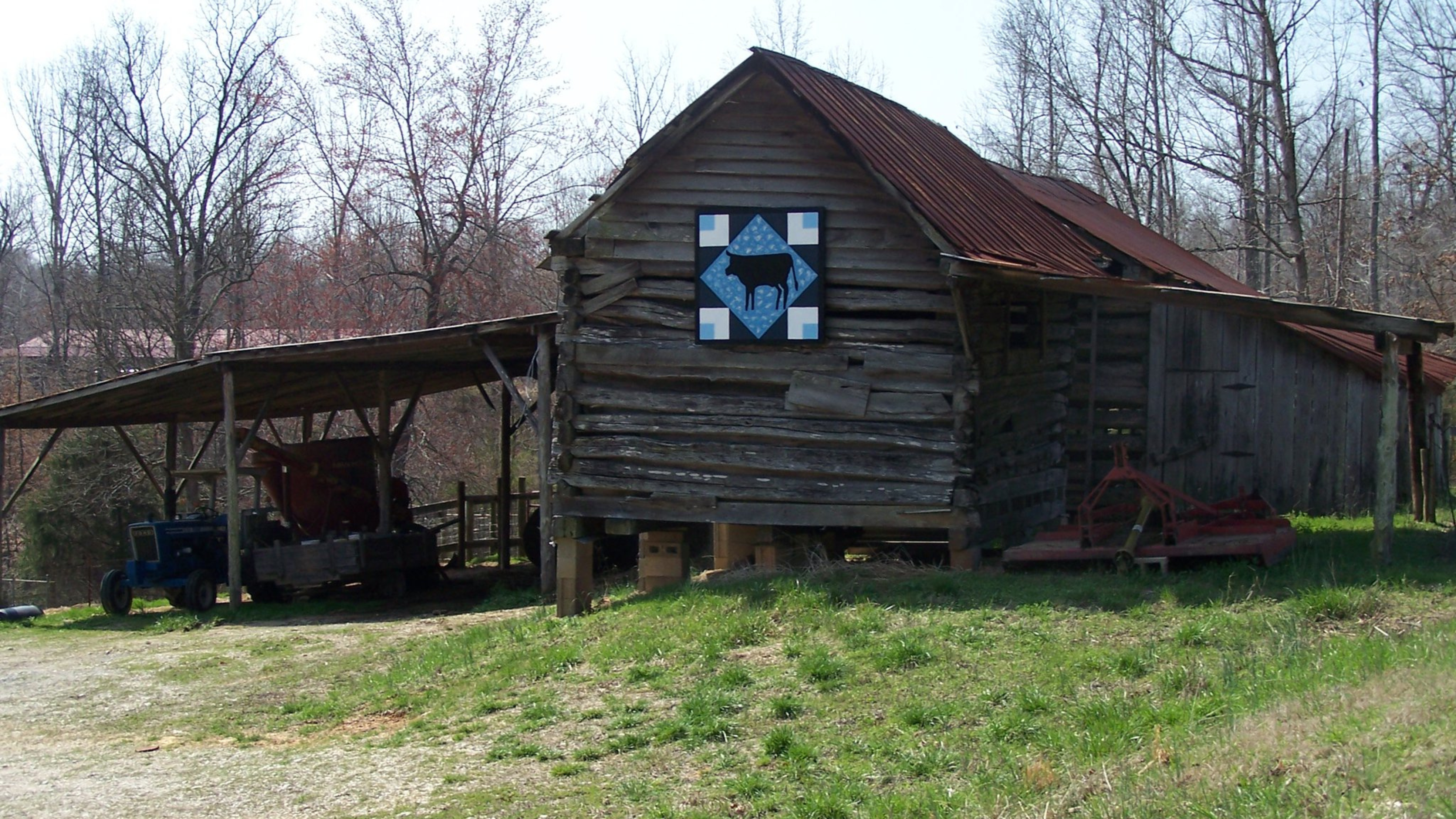 Image of trees an old barn with a blue quilt hanging near the top